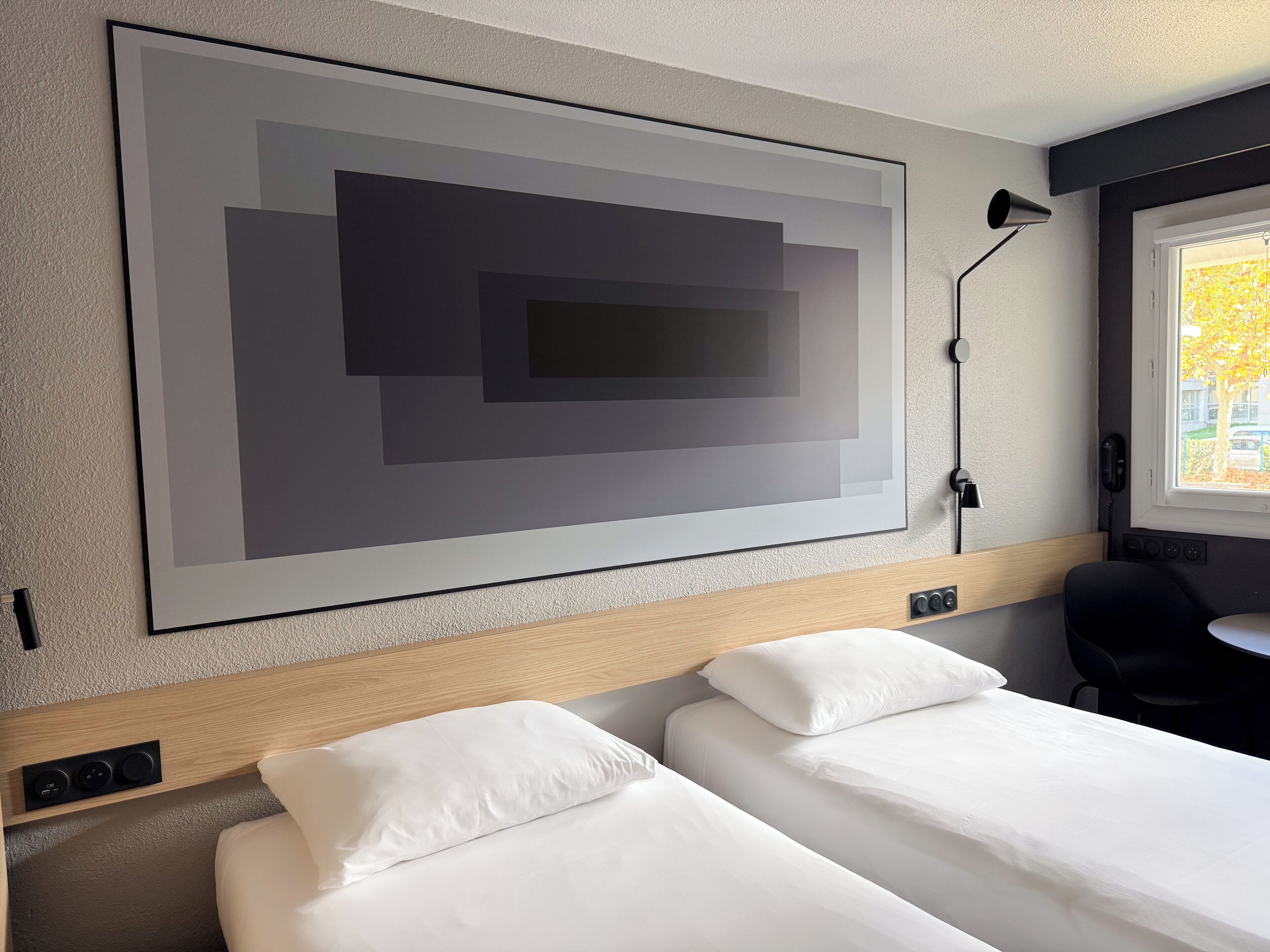 A hotel room with a large abstract painting, a desk, and two beds.