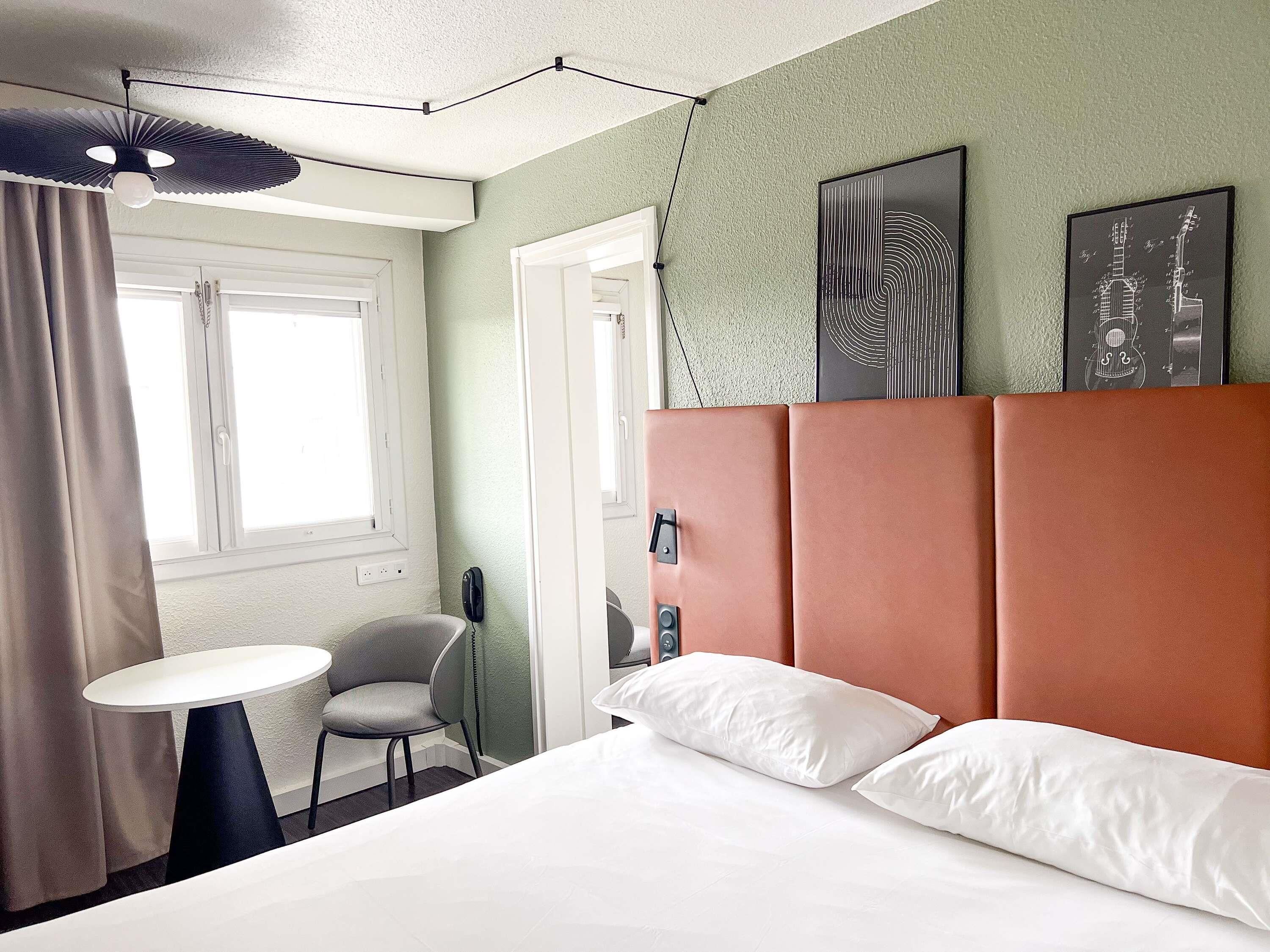 Una habitación de hotel con una cama, una silla, una mesa y obras de arte en la pared.
