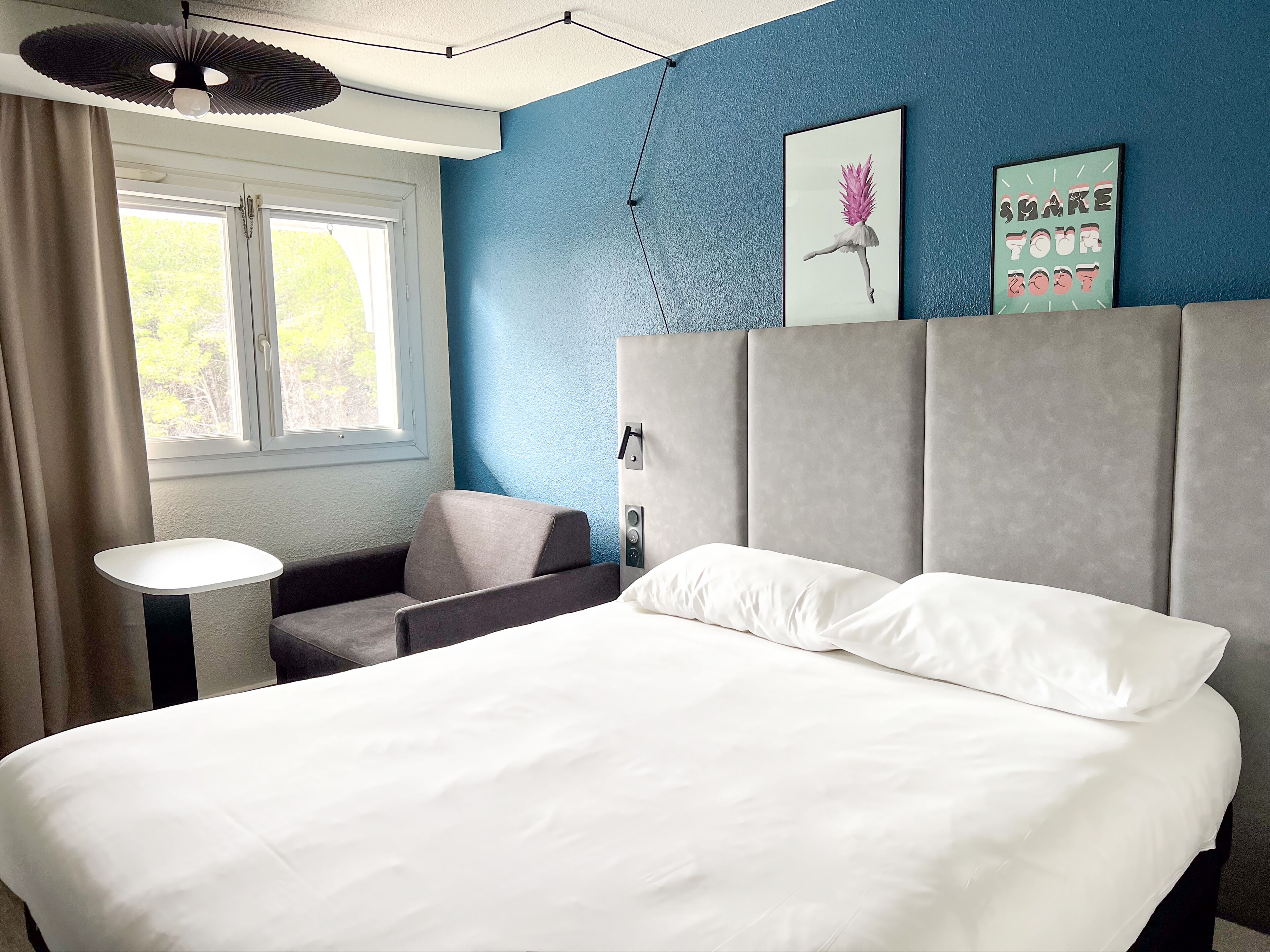 A modern hotel room with a large bed, a small desk, and a window with curtains.