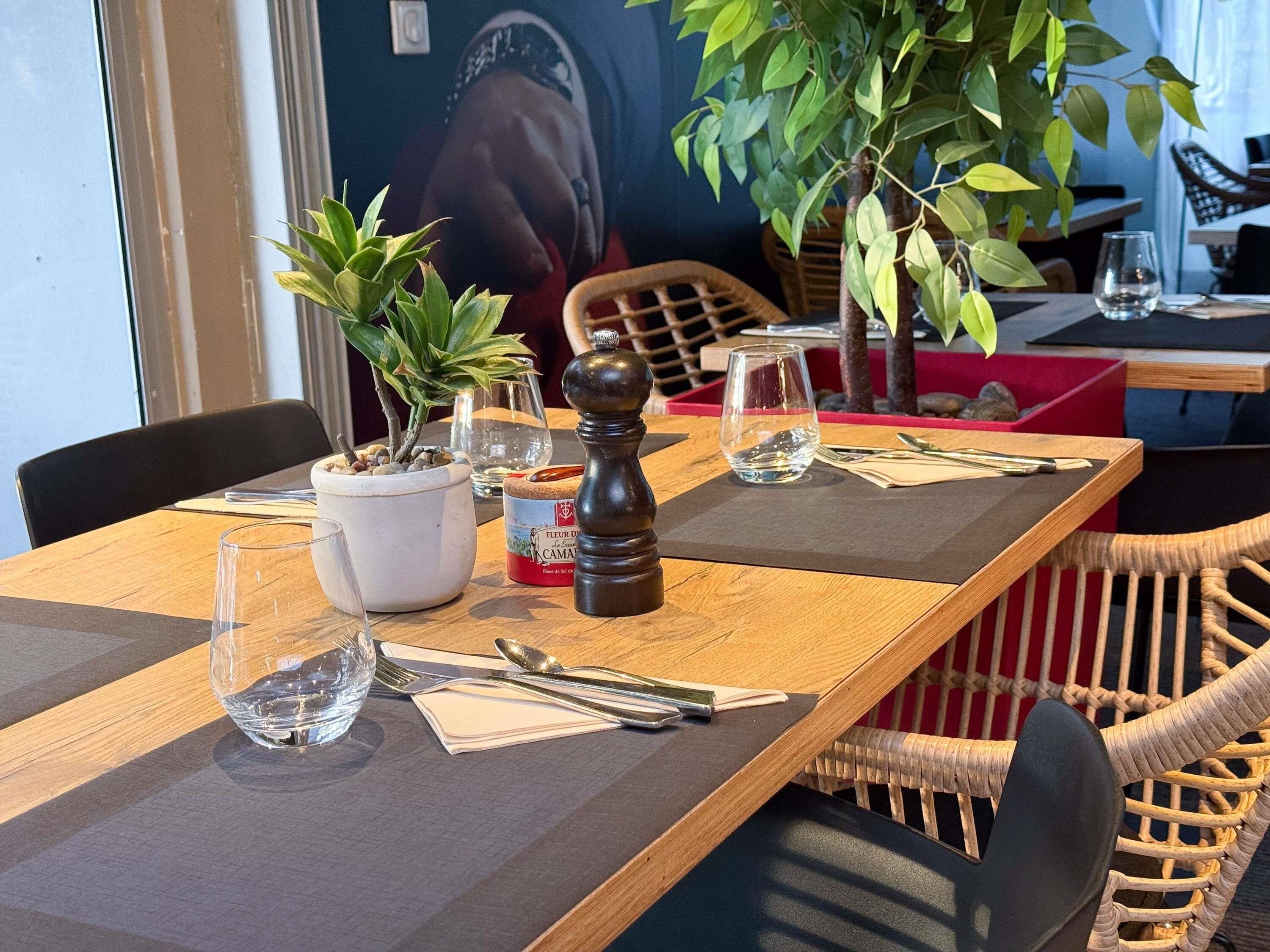Une table à manger dressée avec une plante en pot, des salières et des poivrières, et une bouteille de fleur de sel.