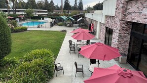 Eine Terrasse mit Sitzgelegenheiten und Sonnenschirmen, im Hintergrund ein Schwimmbecken und ein Backsteinhaus.