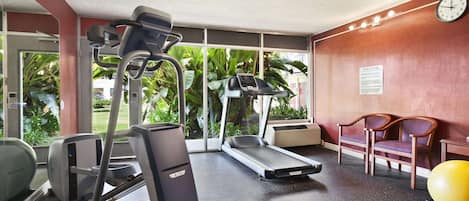 A fitness center with treadmills, a stationary bike, and a rowing machine. There are two wooden chairs and a yellow exercise ball.
