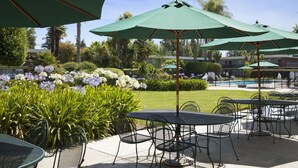 Eine Außenpatio-Terrasse mit runden Tischen und Stühlen, grünen Sonnenschirmen und einem Pool im Hintergrund.