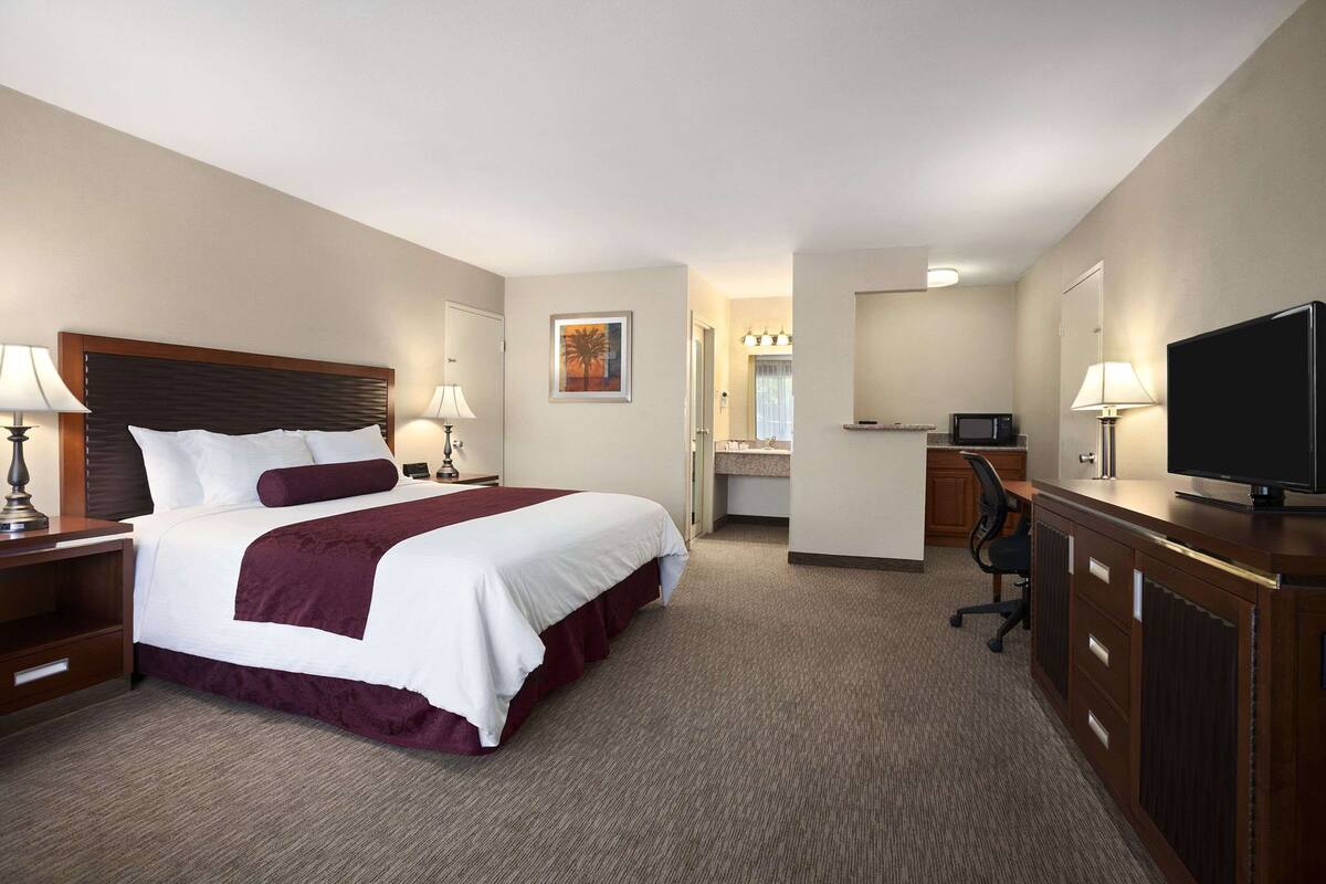 Une chambre d’hôtel avec un grand lit, un bureau avec une télévision, une chaise et une salle de bain visible à travers une porte ouverte.