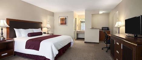 Habitación de hotel con una cama grande, un escritorio con televisor, una silla y un baño visible a través de una puerta abierta.