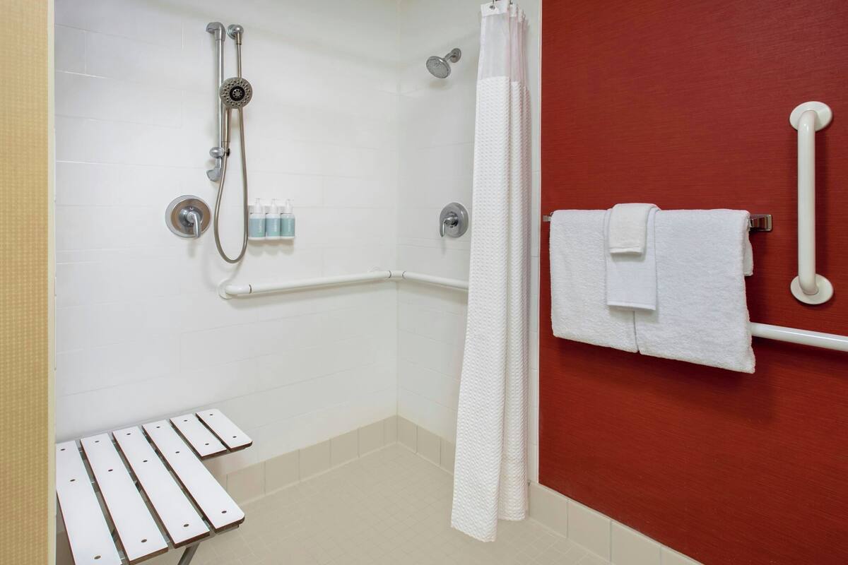 A shower area with a handheld showerhead, a wall-mounted faucet, and a white towel rack with two towels.