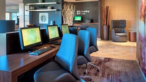 A modern hotel lobby with multiple computer workstations, a seating area with a chair, and a 'Boarding Pass' sign on the wall. - Courtyard by Marriott Mt. Laurel (Mount Laurel)