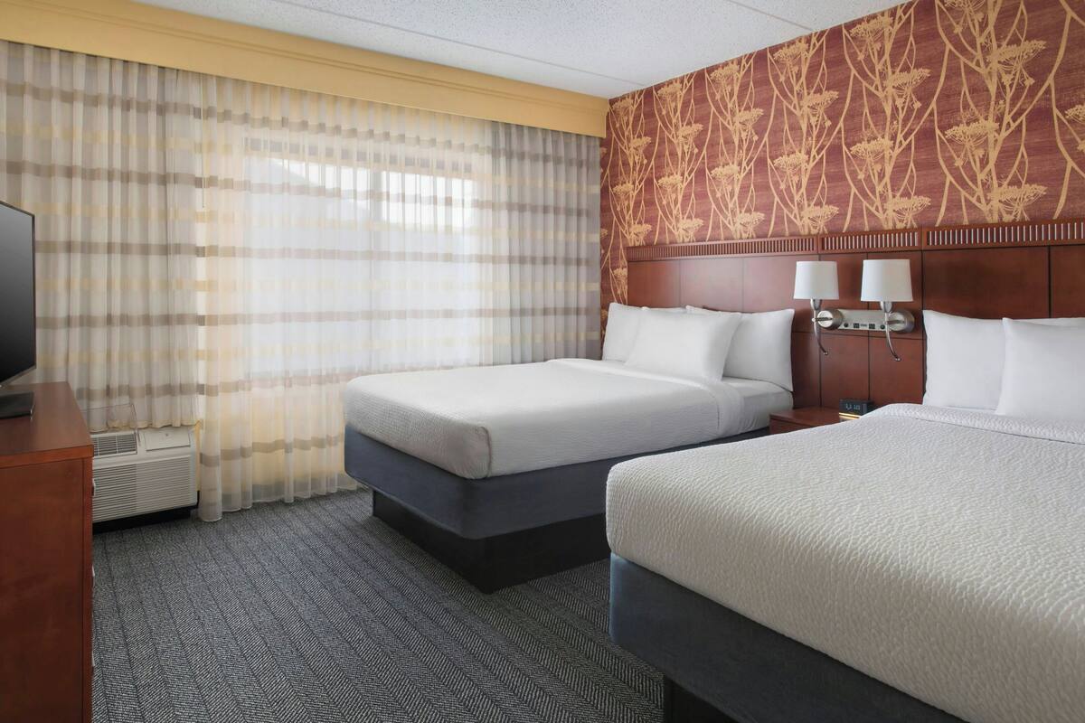 A hotel room with two beds, a TV, a desk, and a window with curtains.