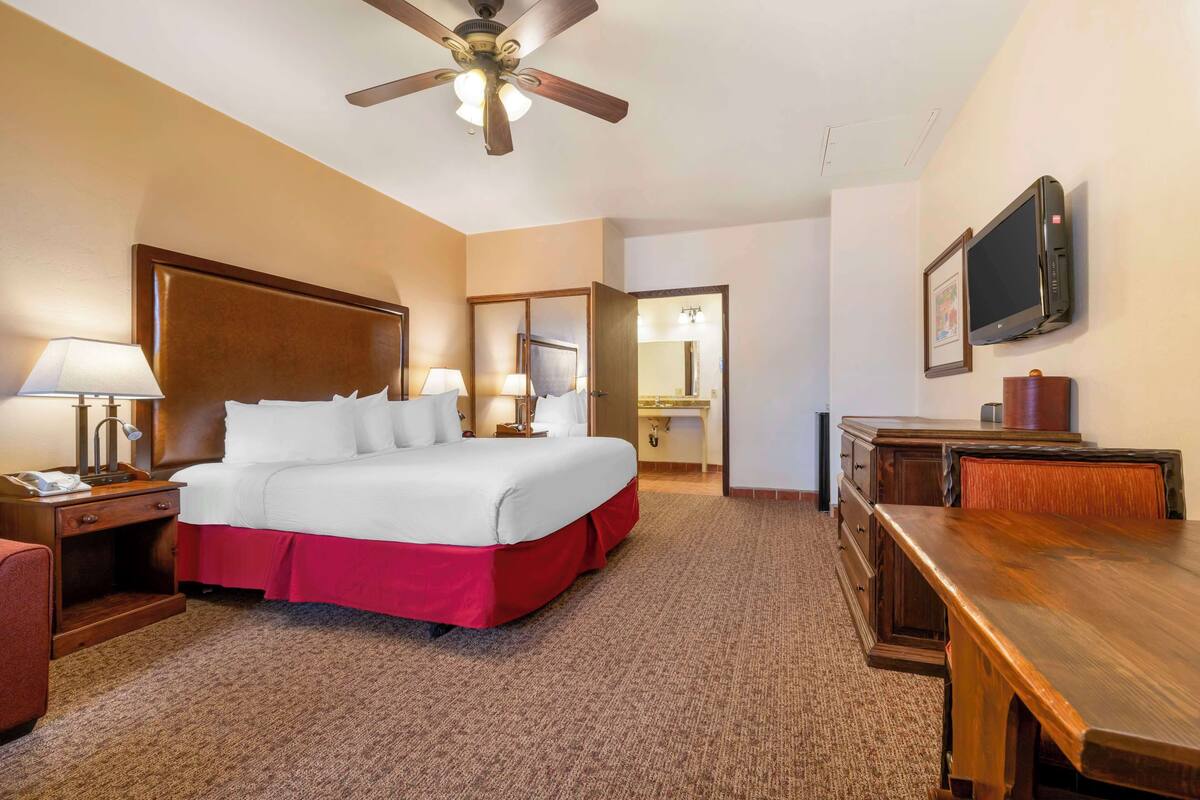 Una habitación de hotel con una cama grande, un escritorio, un televisor y un ventilador de techo.