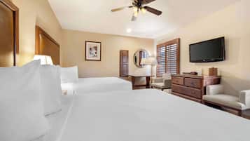 A hotel room with two beds, a ceiling fan, a TV, a dresser, a lamp, and a framed picture on the wall.