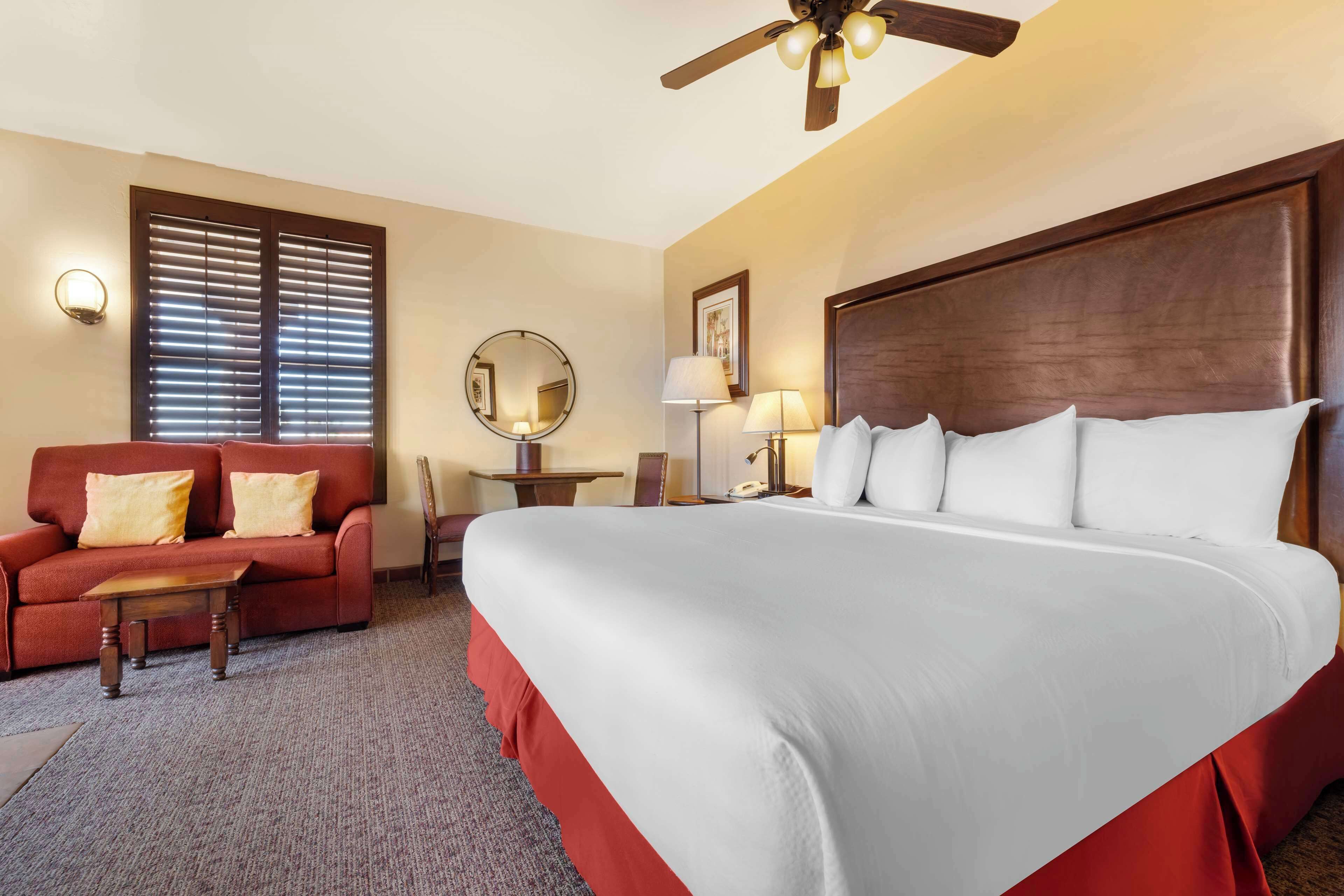 Une chambre d’hôtel avec un grand lit, un canapé rouge, une petite table et un ventilateur de plafond.