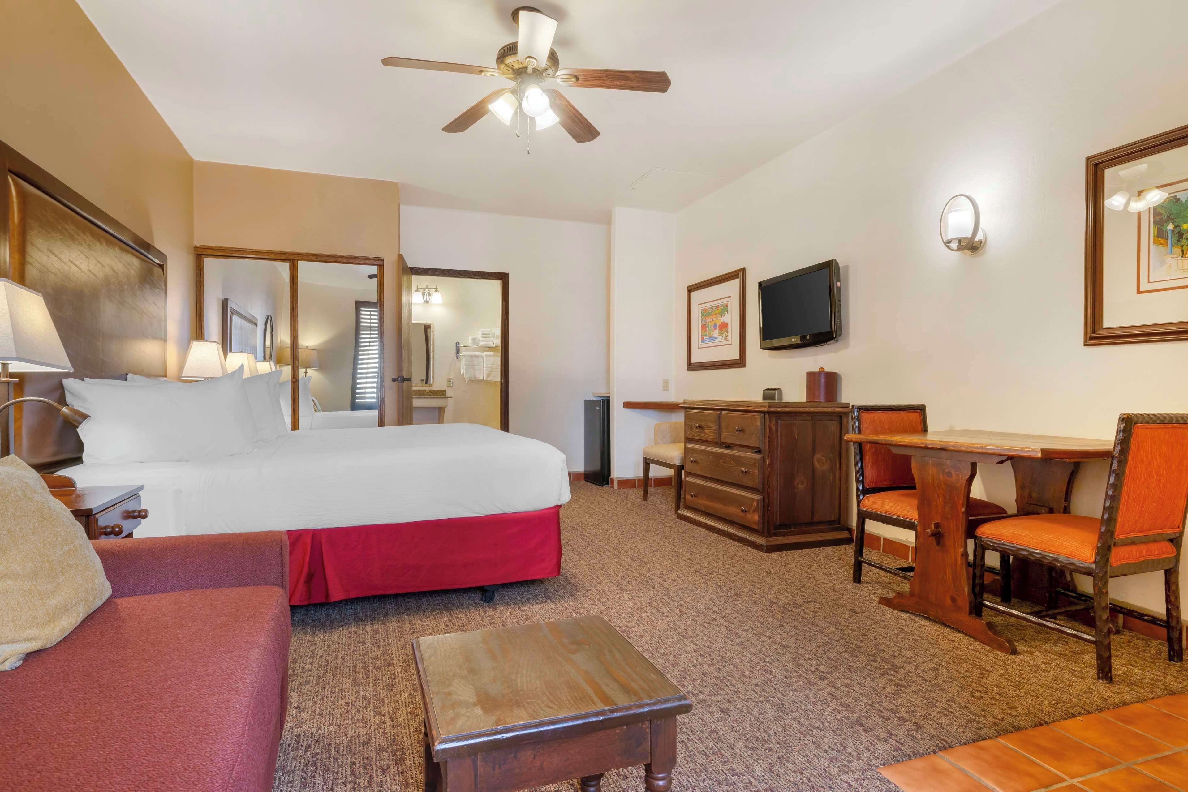 A hotel room with a bed, a desk, a chair, a television, and a ceiling fan.