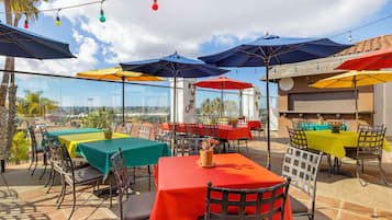 An outdoor dining area with tables and chairs, umbrellas, and a view of the city.
