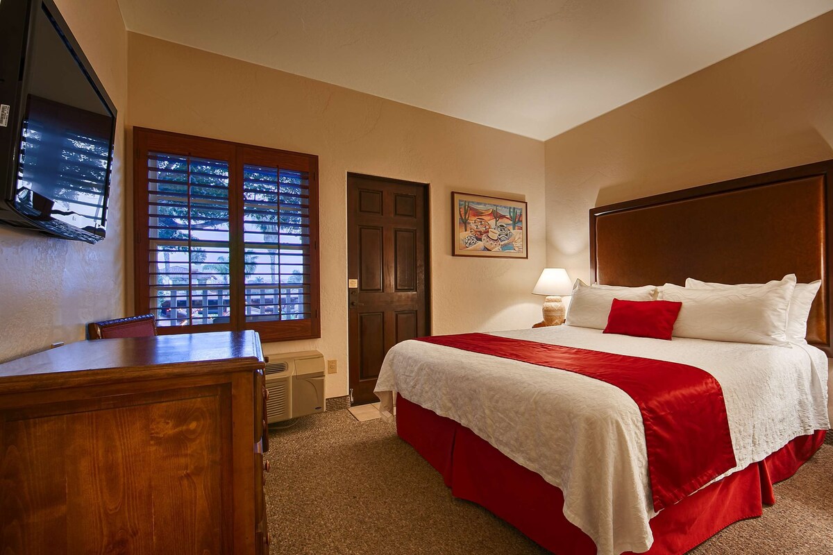 Habitación de hotel con una cama grande, cabecera de madera, escritorio y ventana con persianas.