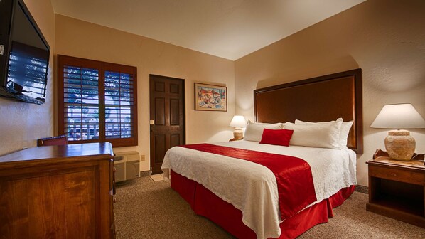 Habitación de hotel con una cama grande, cabecera de madera, escritorio y ventana con persianas.