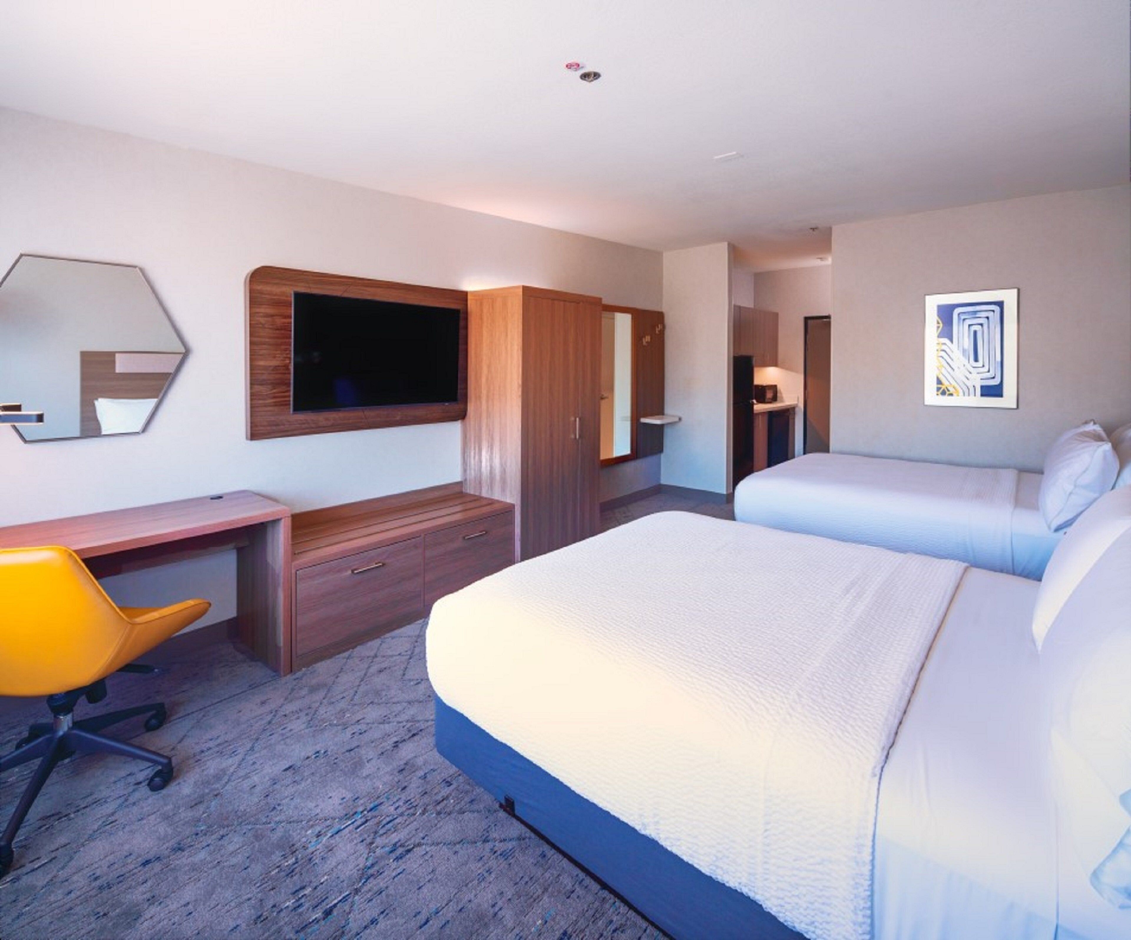 A hotel room with a bed, a desk, a chair, a wardrobe, and a television mounted on the wall.