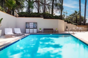 A clear blue pool with lounge chairs and a bench, surrounded by a low wall and greenery. - Holiday Inn Express La Mesa Near SDSU by IHG (San Diego)