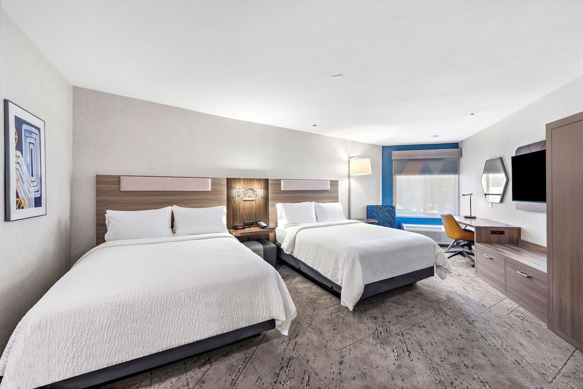 A hotel room with two beds, a desk, a chair, a TV, and a window.