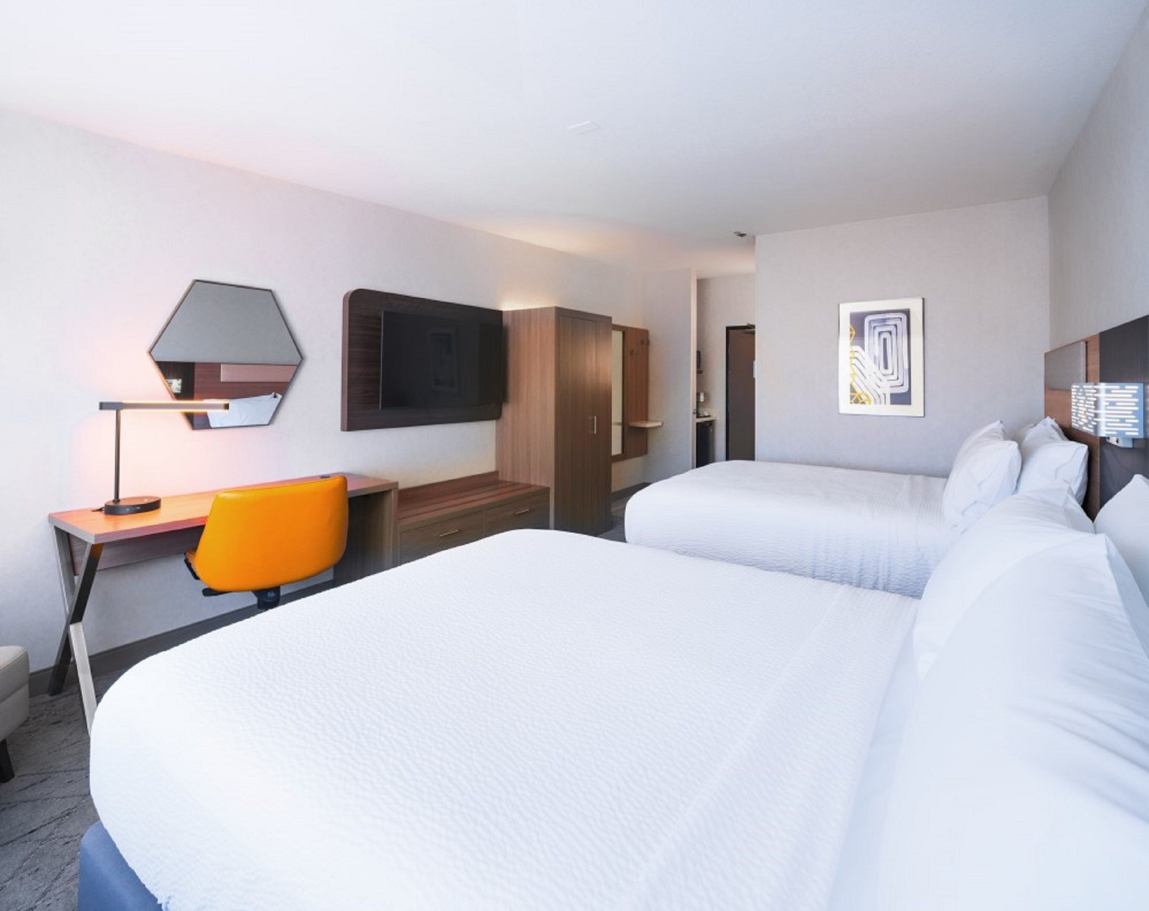 A hotel room with two beds, a desk with a chair, a TV, and a framed picture on the wall.
