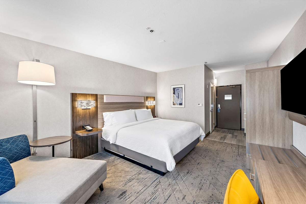 A modern hotel room with a bed, bedside table, lamp, and a flat-screen TV.