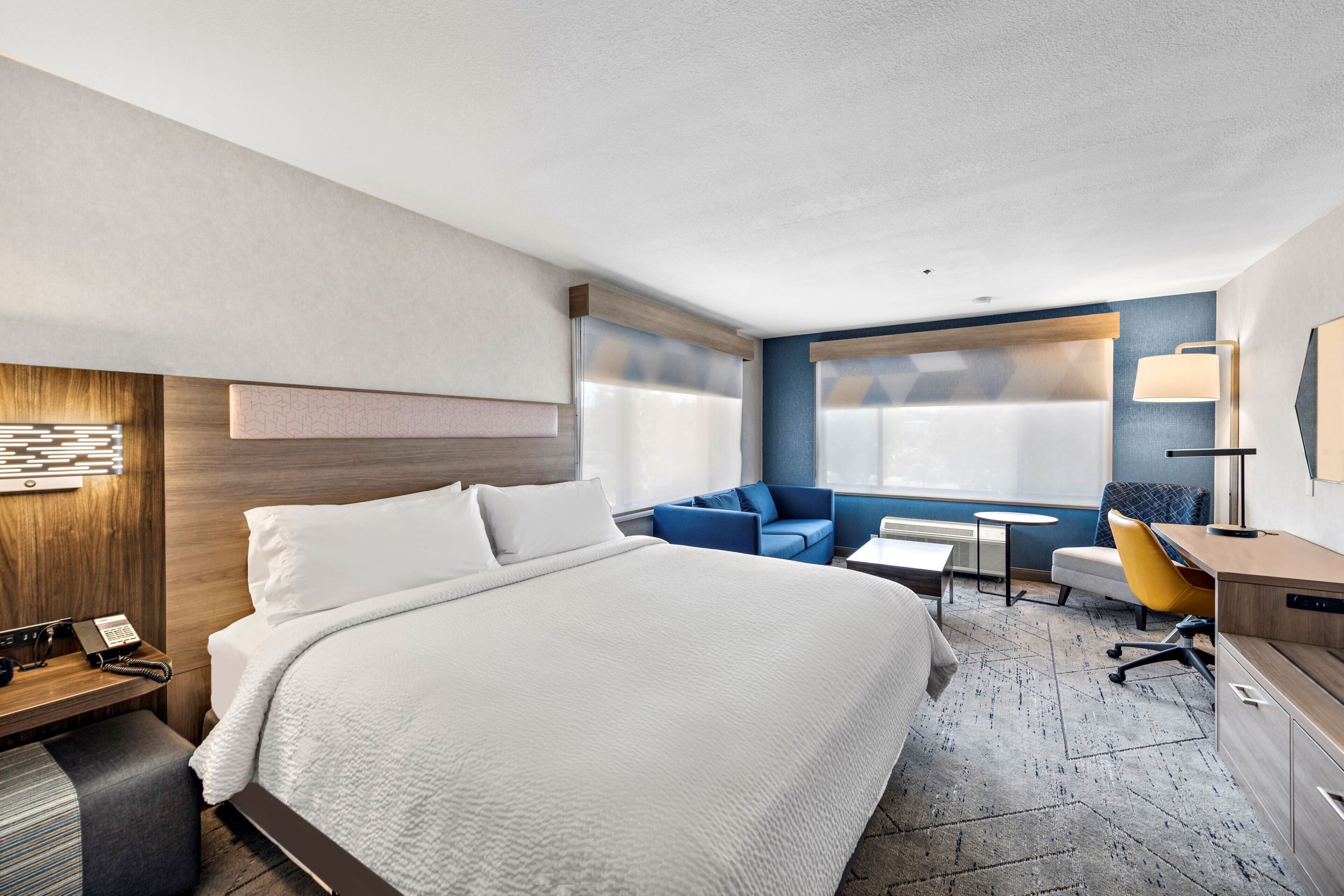 A hotel room with a bed, a desk, a chair, a sofa, and a window.