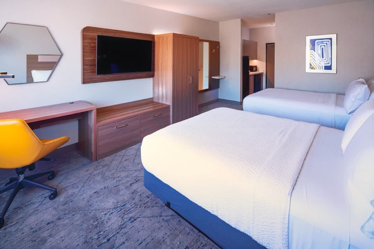A hotel room with a bed, a desk, a chair, a wardrobe, and a television.