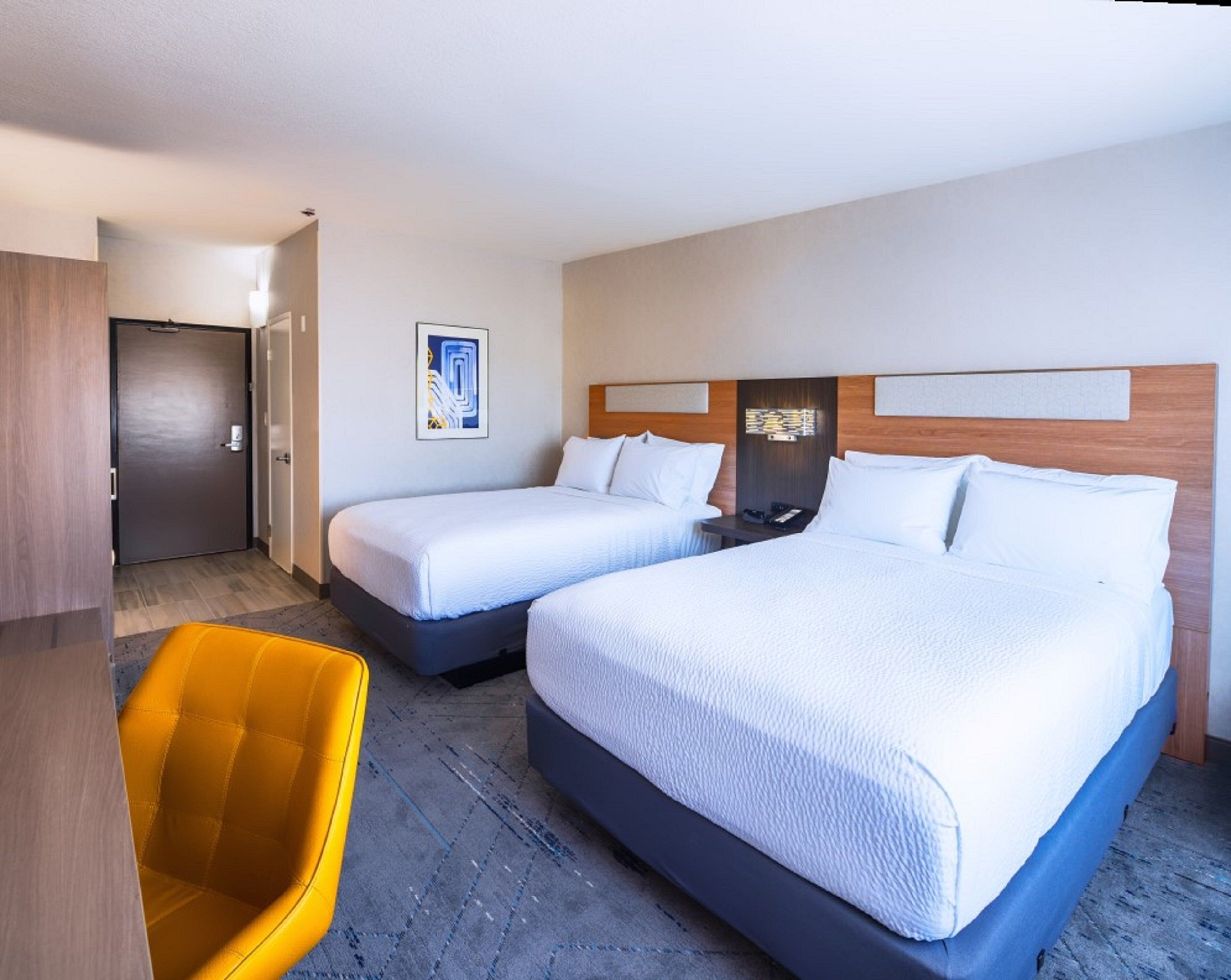 Una habitació d'hotel amb dos llits, un escriptori, una cadira i una porta.