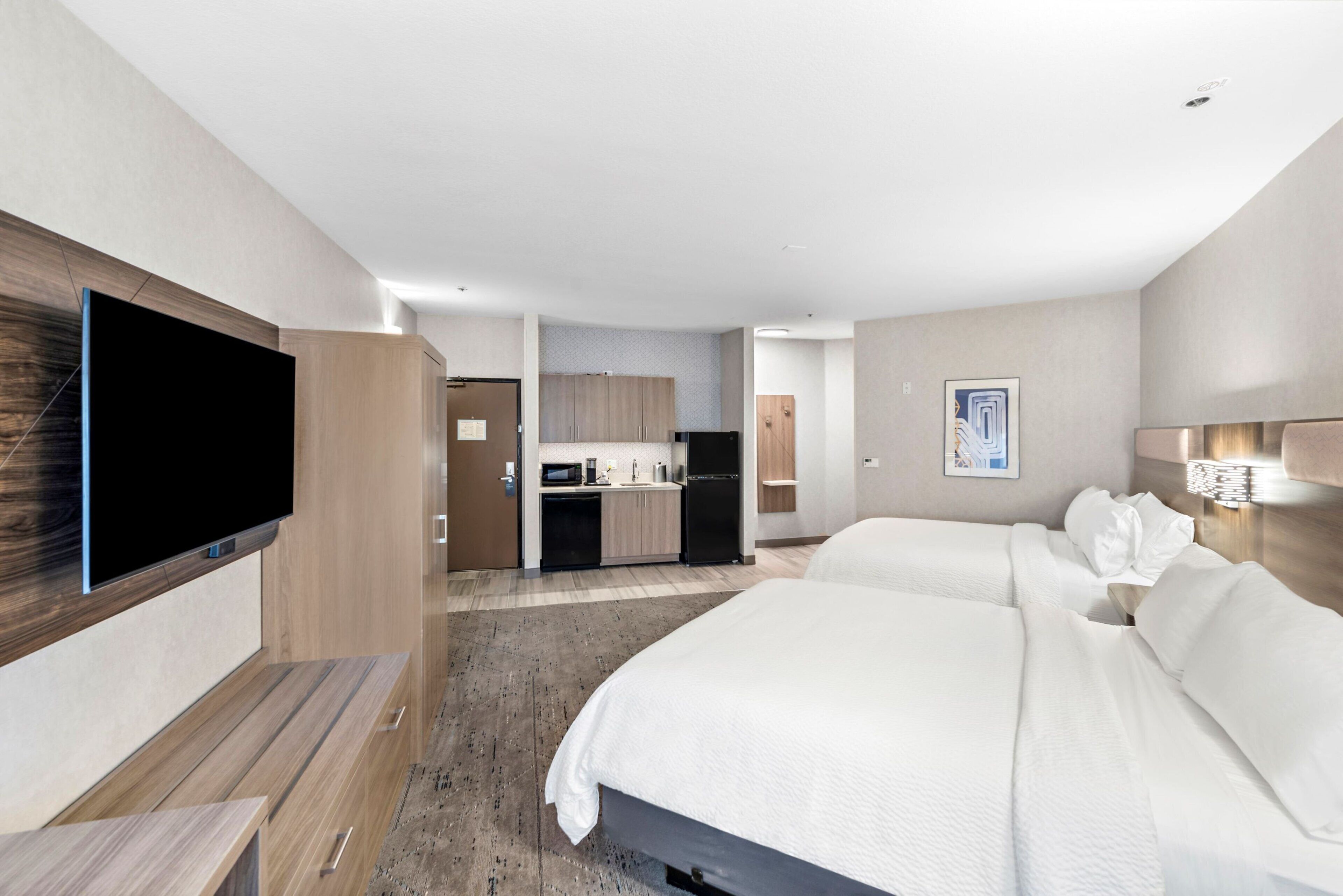 A hotel room with a flat-screen TV, a bed, a desk, and a kitchenette.