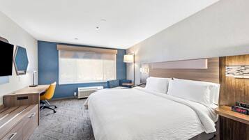 A hotel room with a large bed, a desk, a chair, a TV, and a window.