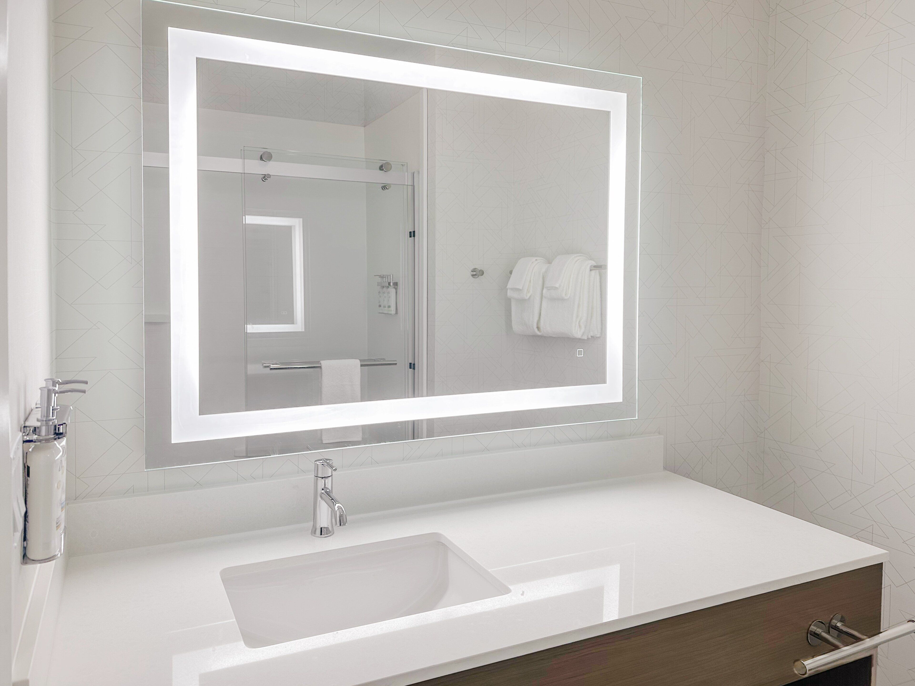 A modern bathroom with a large mirror, a white sink, and a towel rack.