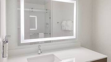 A modern bathroom with a large mirror, a white sink, and a towel rack.