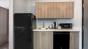 Une cuisine compacte équipée d’un réfrigérateur noir, d’un four à micro-ondes, d’une machine à café et d’un lave-vaisselle.