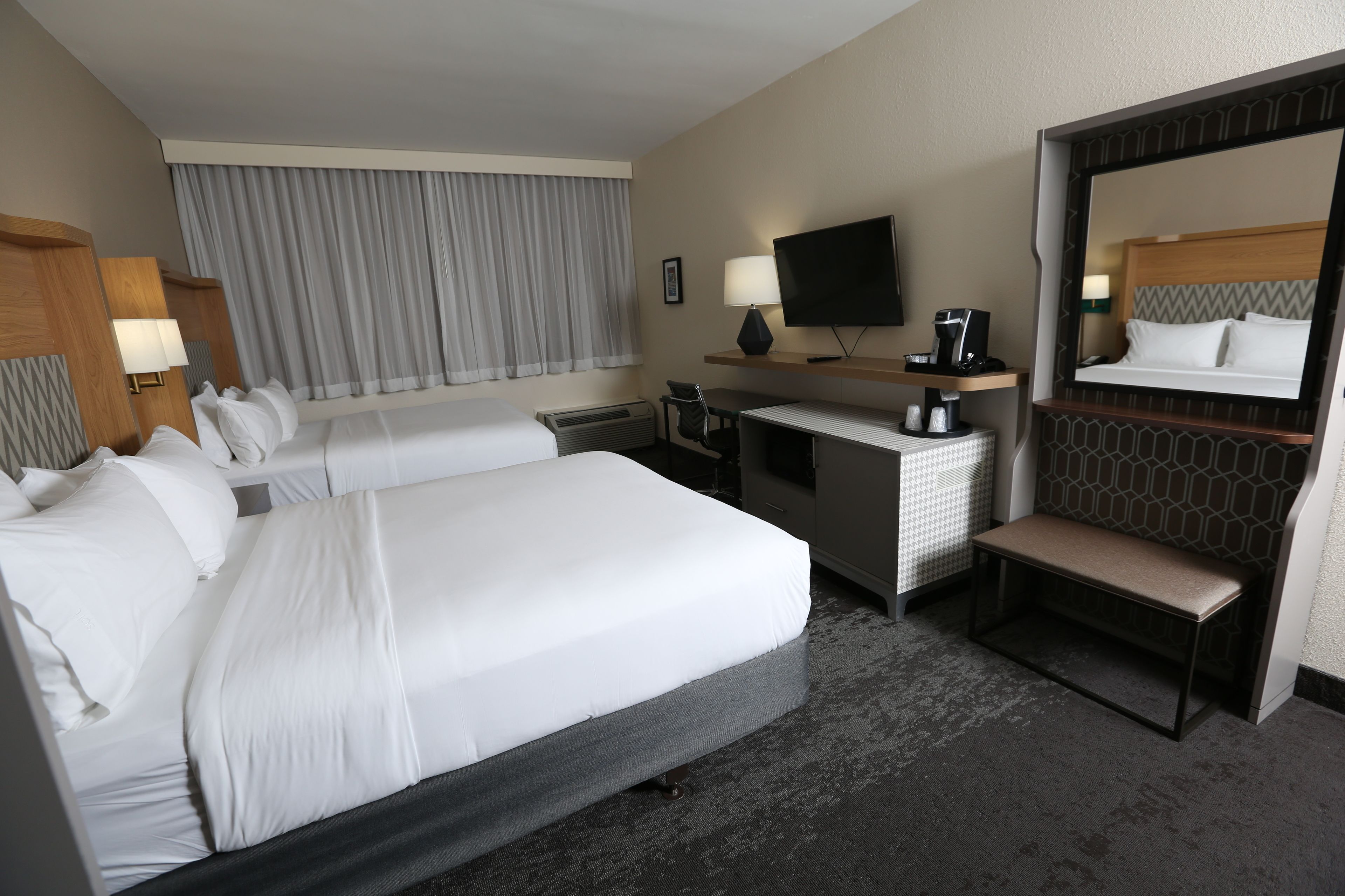 A hotel room with two beds, a desk, a TV, and a large mirror.