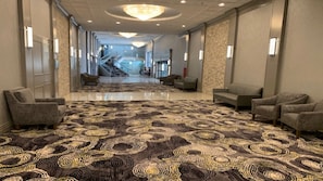 Un hall de hotel con alfombra estampada, zona de estar y una escalera que lleva a otras plantas.