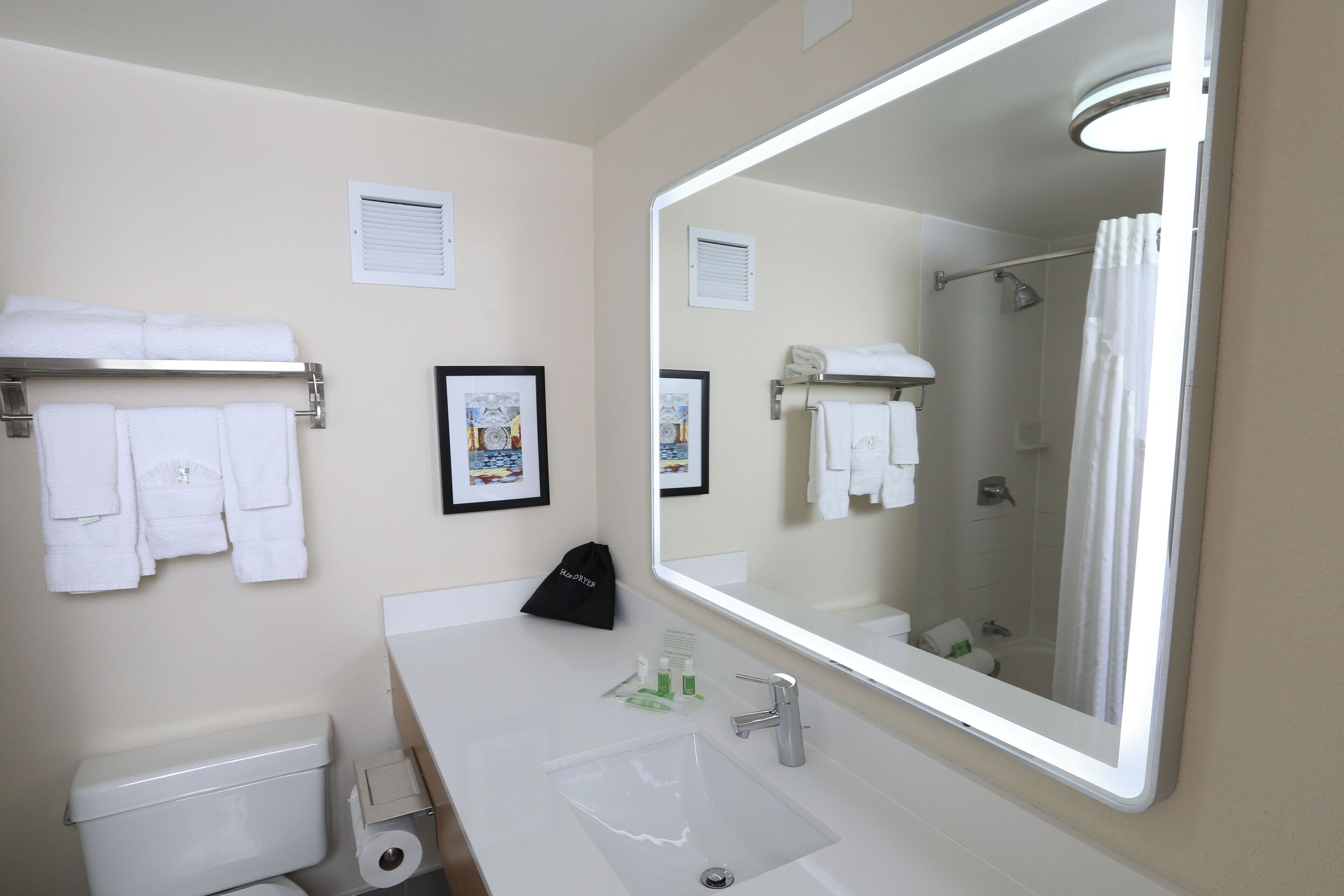 A bathroom with a large mirror, white towels, a toilet, and a sink.