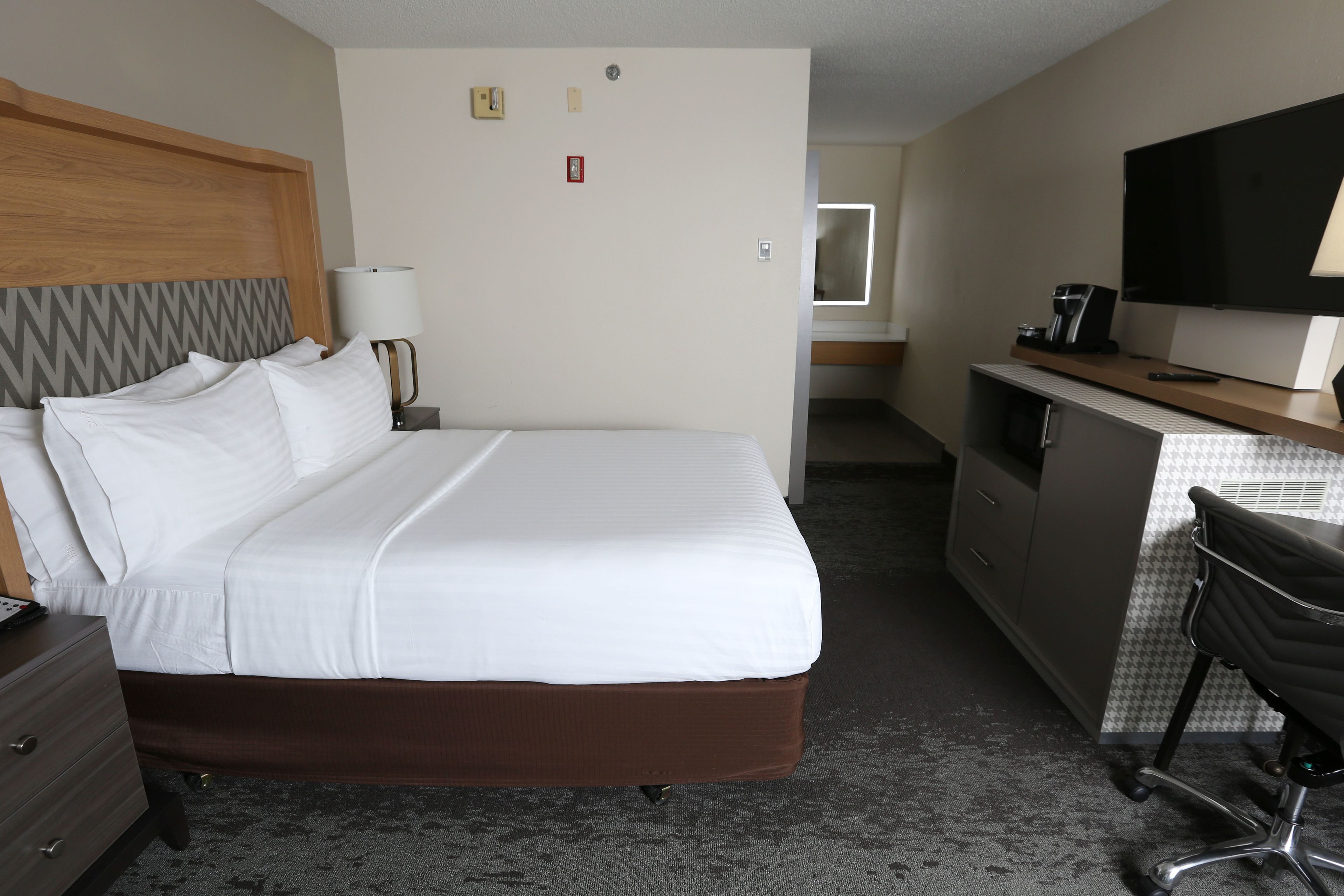 A hotel room with a large bed, a desk with a television, a chair, and a dresser.