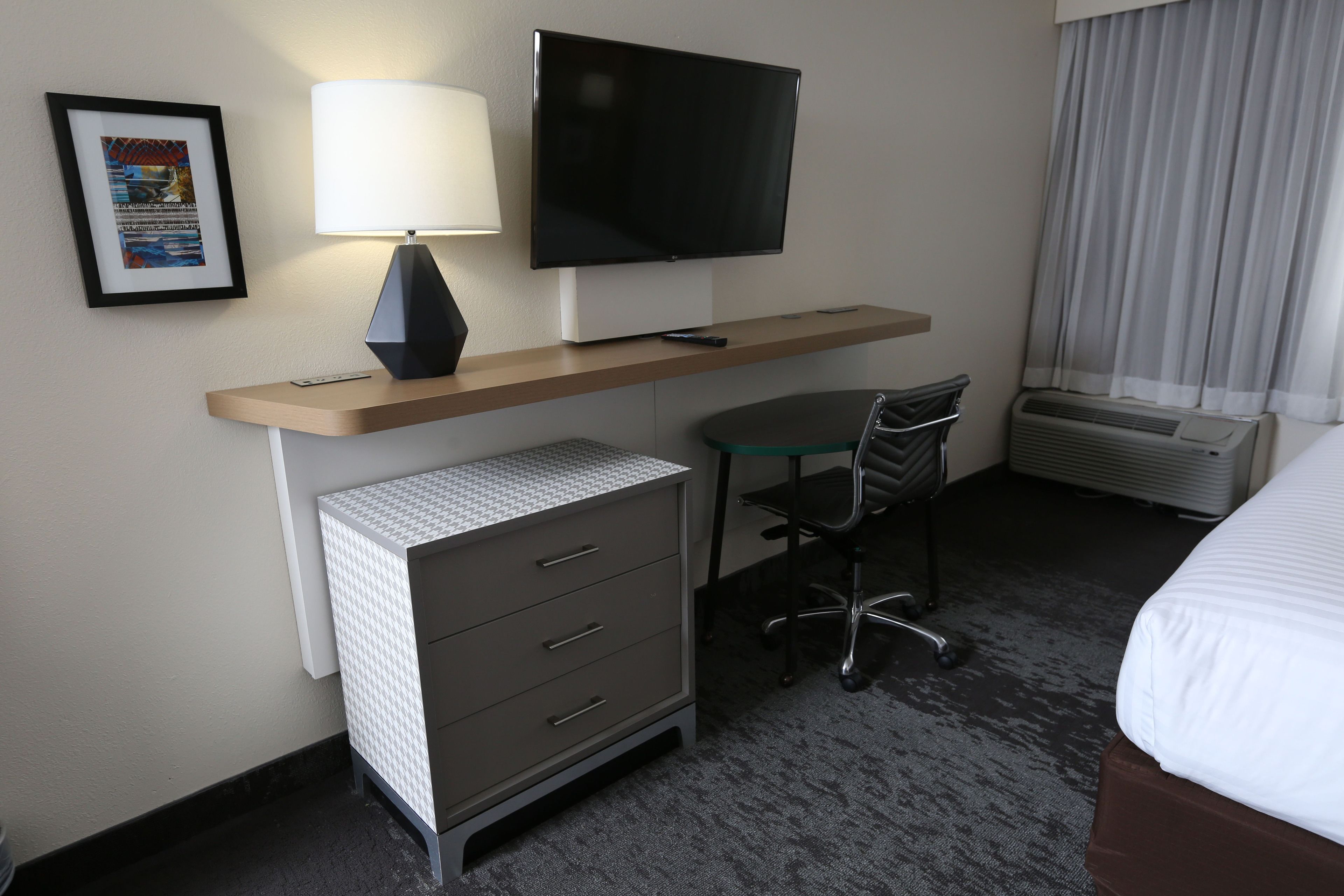 A hotel room with a desk, chair, TV, and a bed.