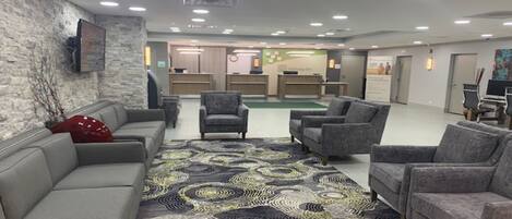 A lobby with a grey sofa, armchairs, a patterned rug, and a reception desk.