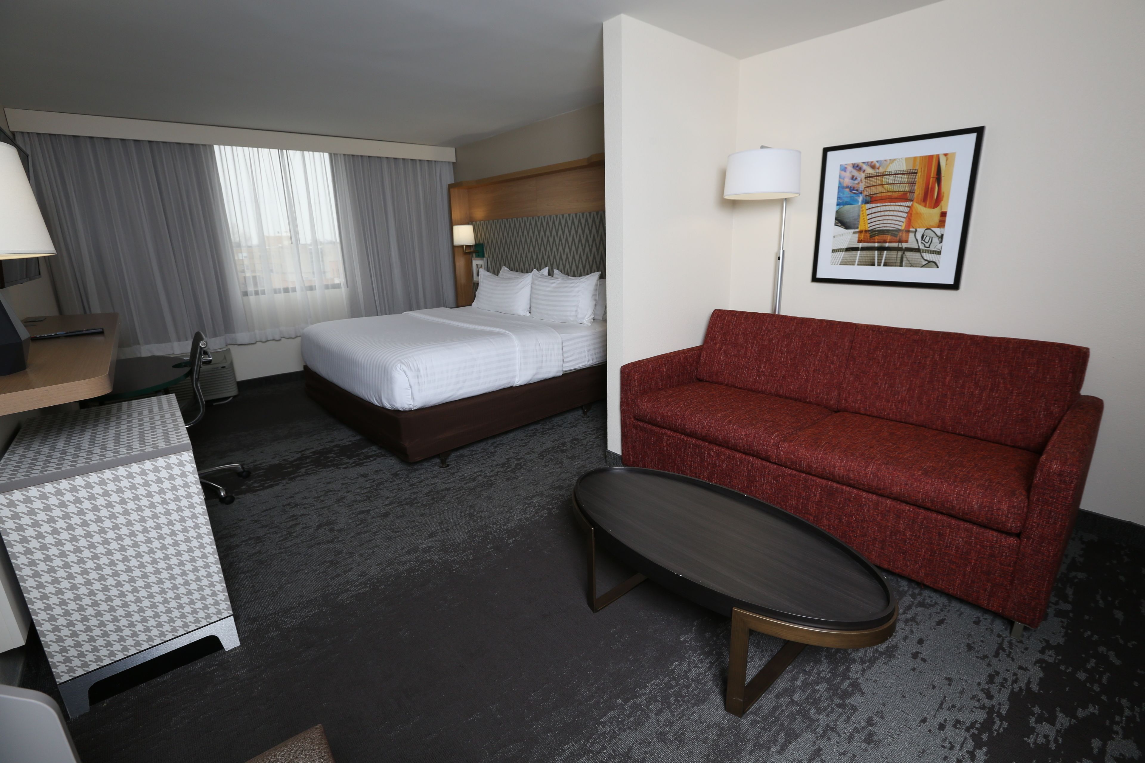Ein Hotelzimmer mit einem Bett, einem roten Sofa, einem Schreibtisch mit Lampe und einem kleinen Tisch.