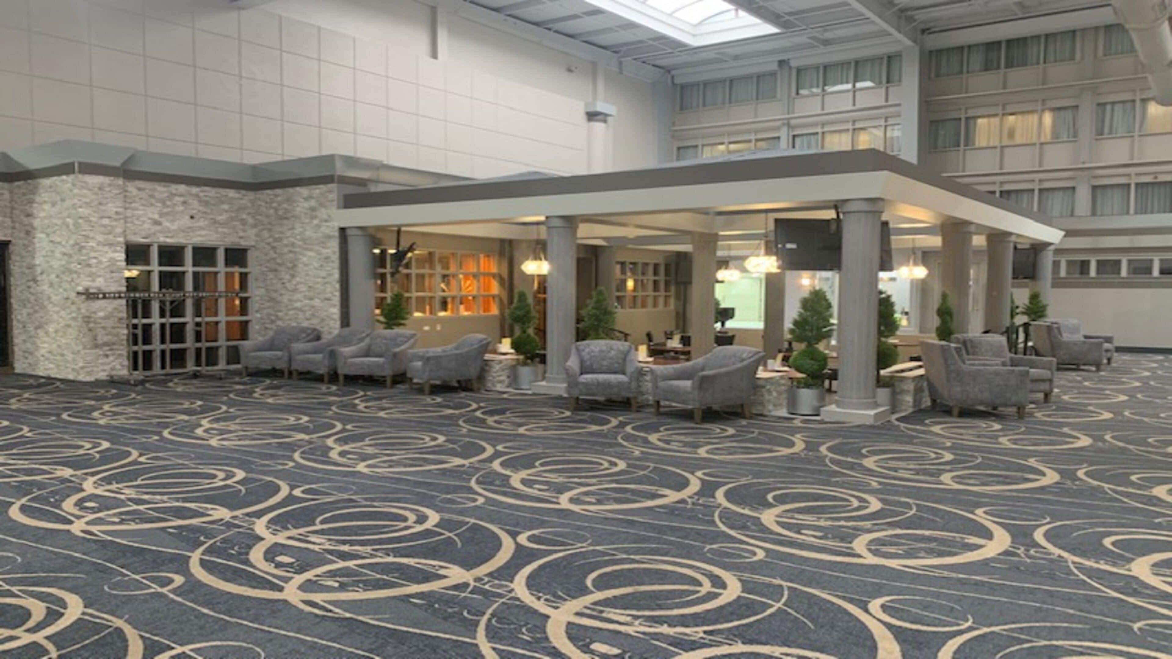 A spacious lobby with a patterned carpet, seating area with armchairs, and a stone accent wall.