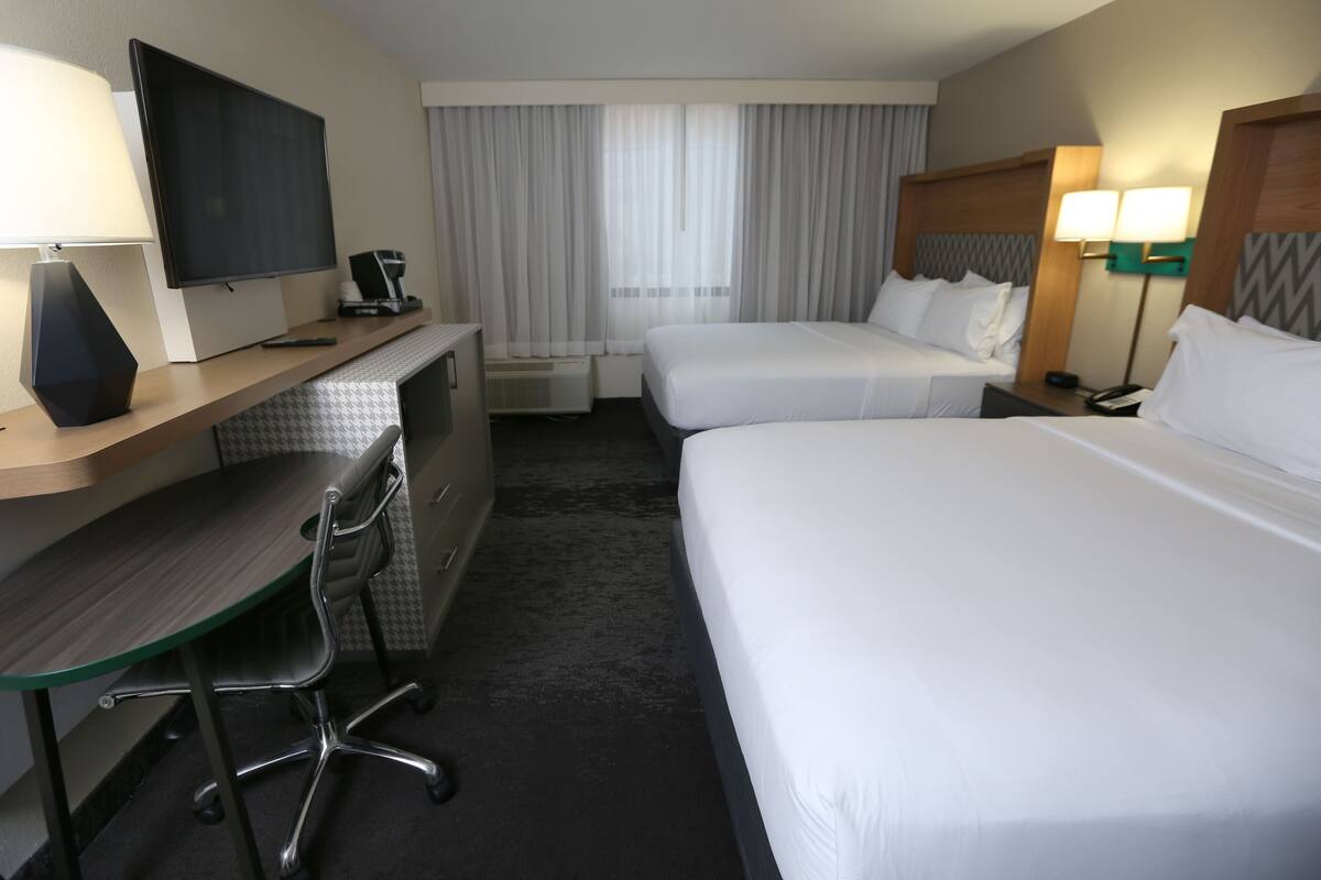 A hotel room with a desk, two beds, a TV, and a window with curtains.