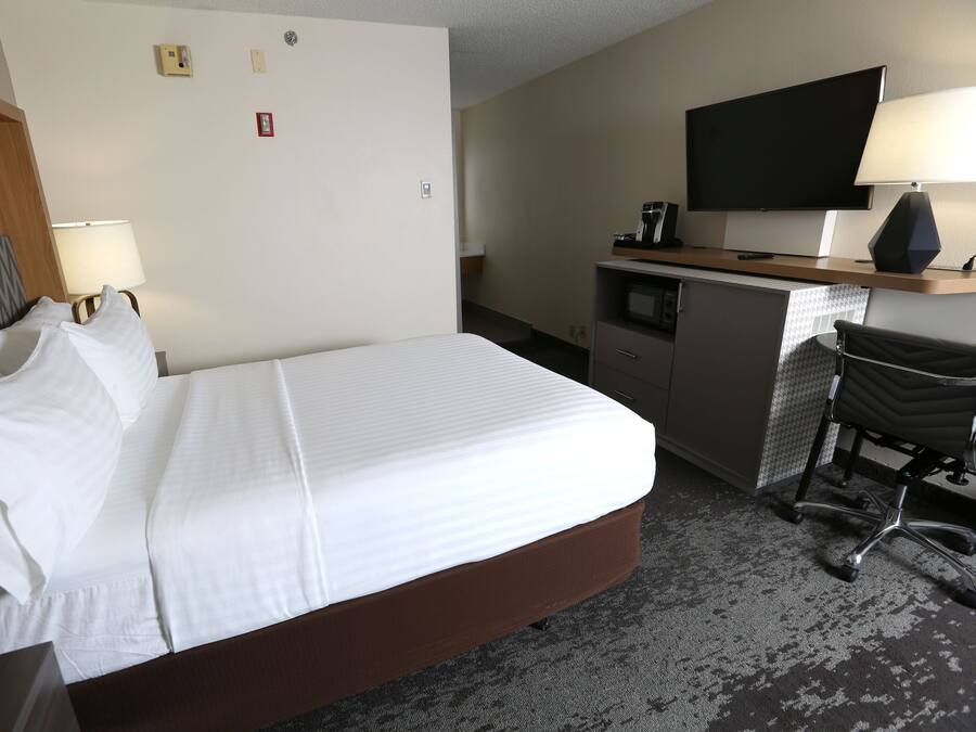 Quarto de hotel com cama, escrivaninha com televisão, cadeira e abajur.