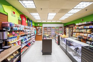 Interior de un supermercado con estantes llenos de productos varios, una zona de cajas y una exhibición de camisetas deportivas.