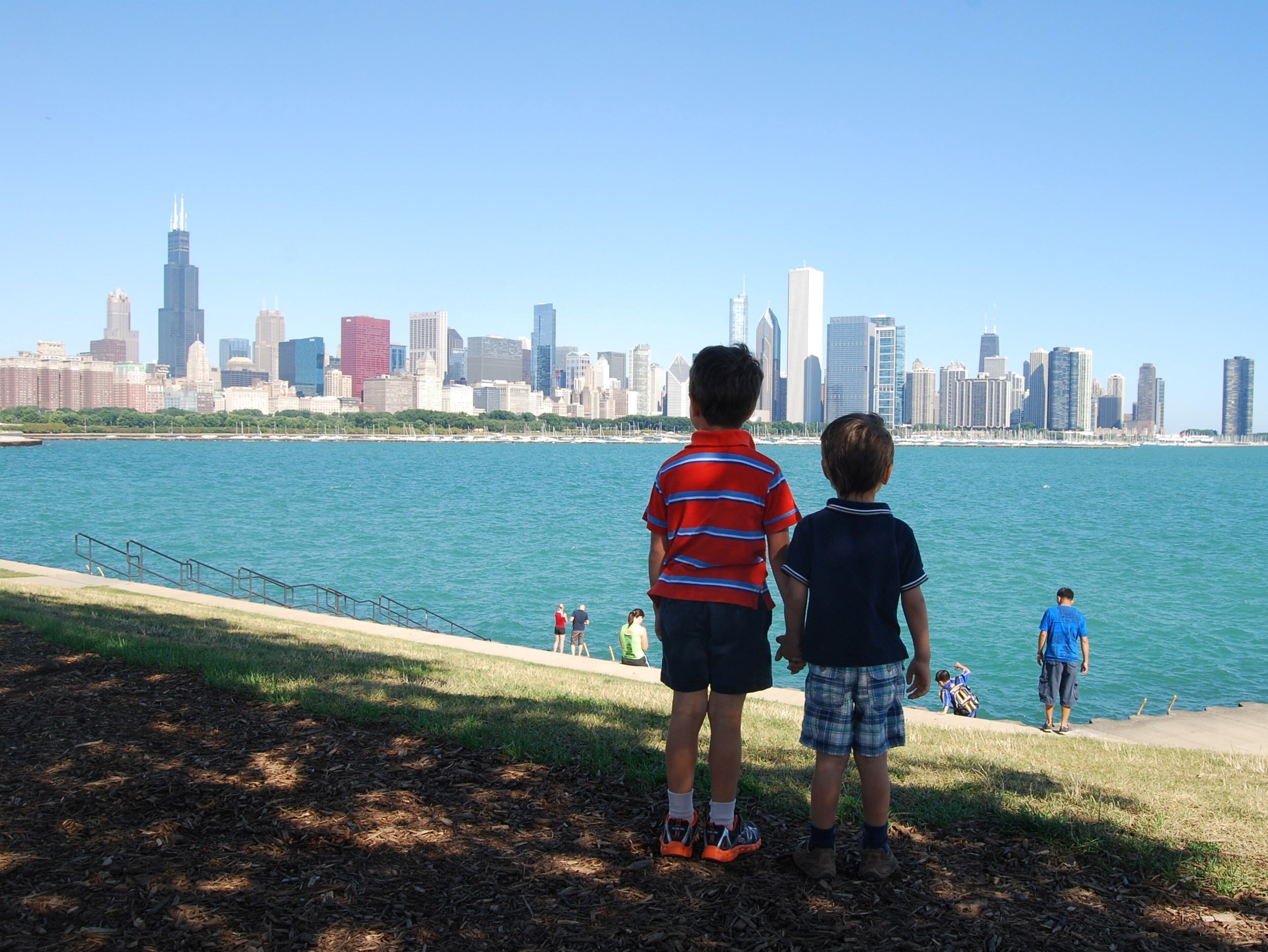Two children standing by a waterfront with a city skyline in the background.