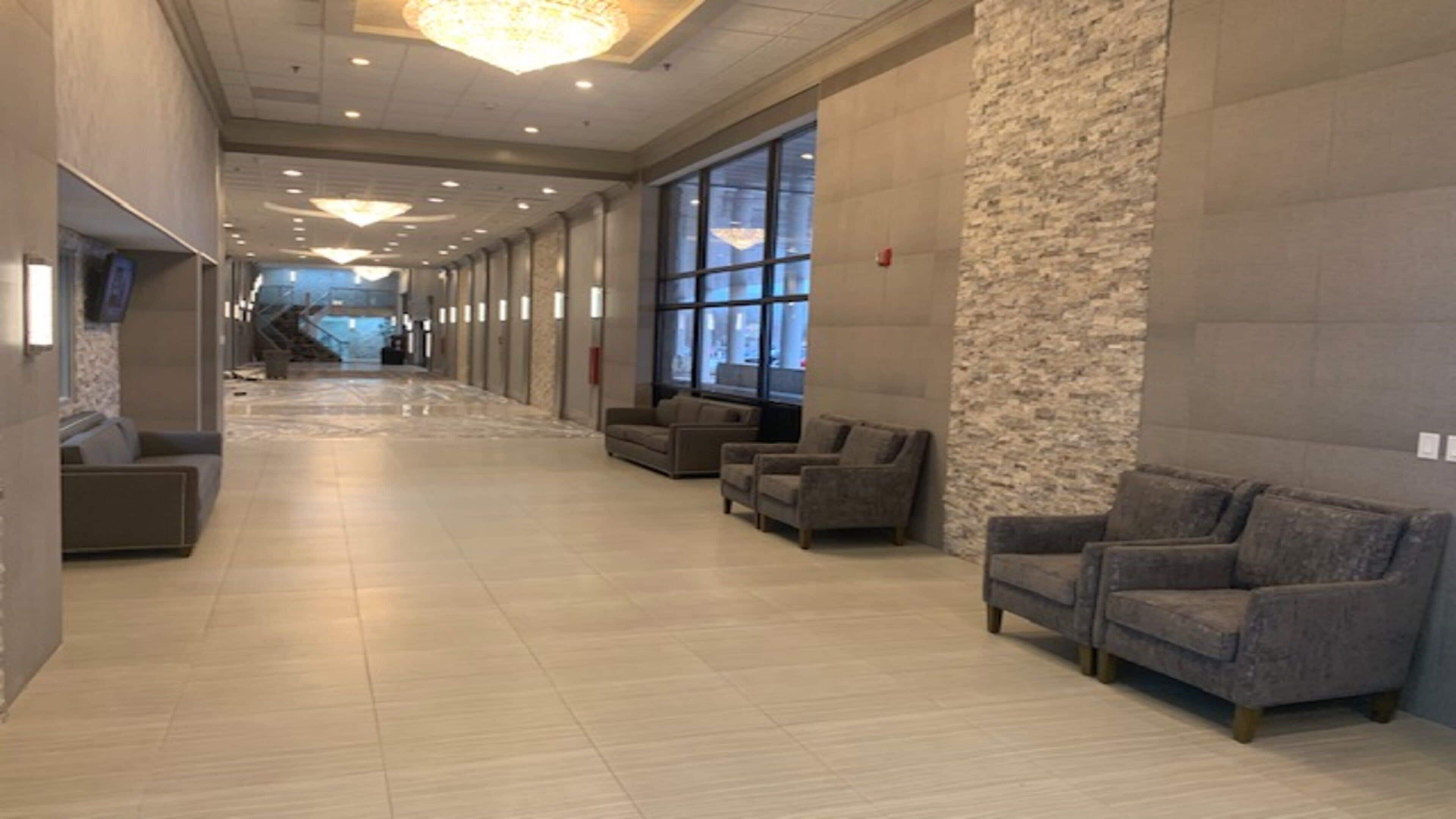 Un hall de hotel con un largo pasillo, una zona de estar con sofás, ventanas amplias y un candelabro.