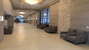 Un hall de hotel con un largo pasillo, una zona de estar con sofás, ventanas amplias y un candelabro.