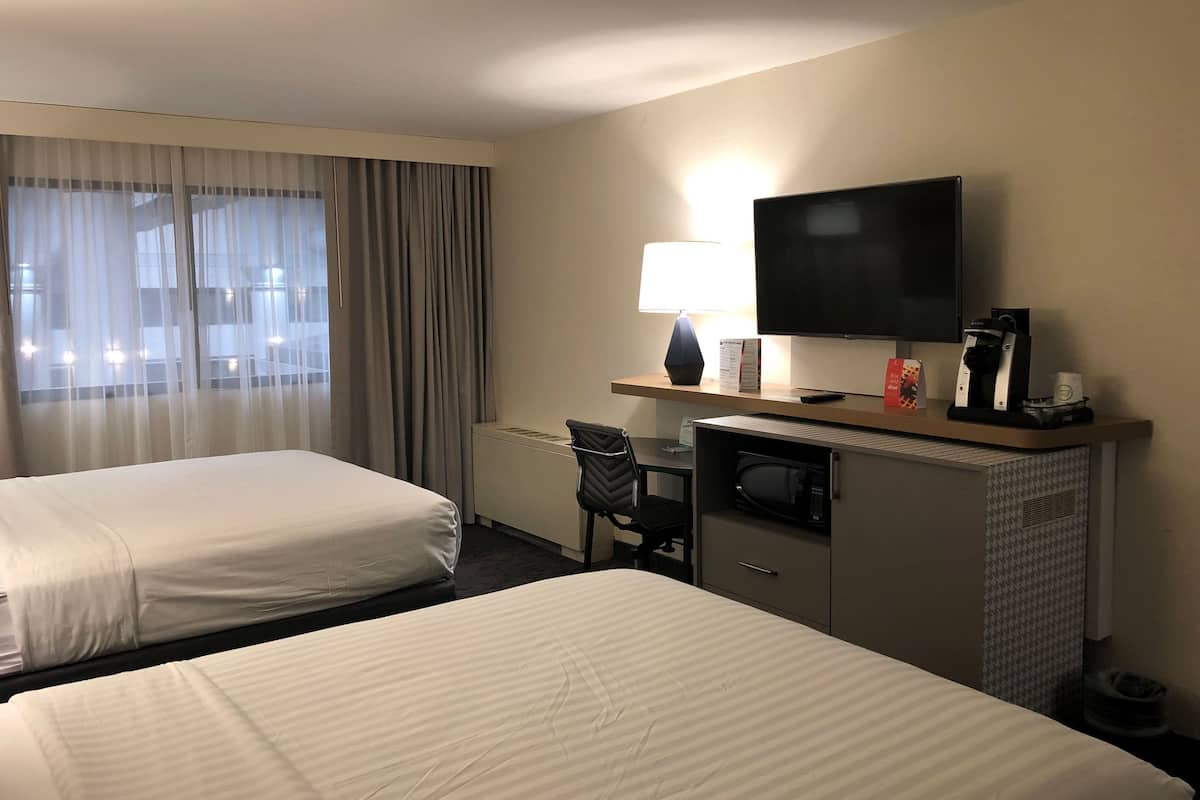 A hotel room with two beds, a desk with a lamp, a TV, and a coffee maker.