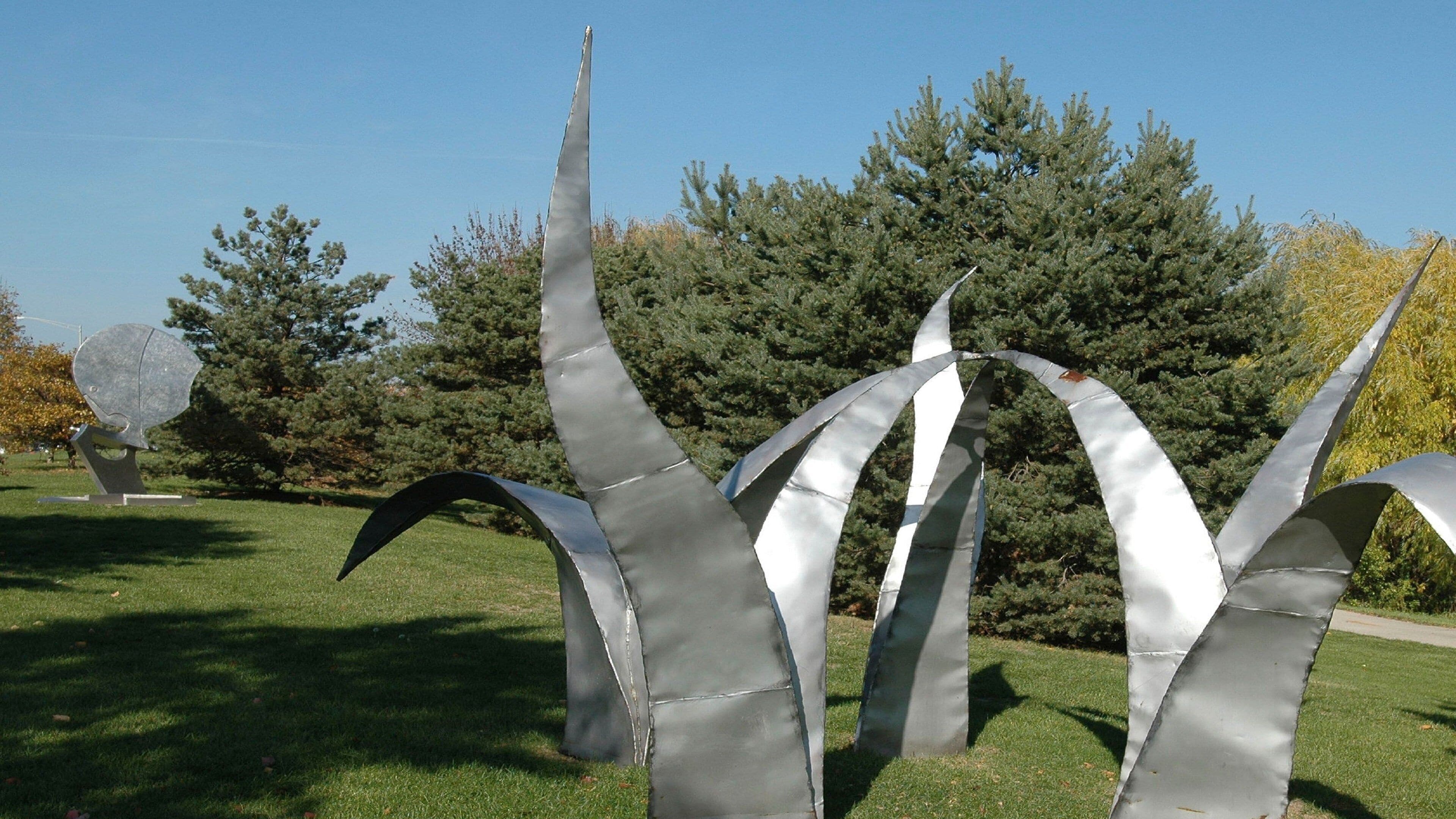 A sculpture garden with abstract metal sculptures and a backdrop of trees.