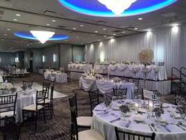 Un salón de banquetes con mesas redondas dispuestas para un evento formal, con manteles blancos, centros de mesa florales e iluminación con velas.