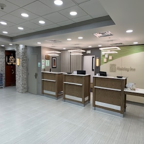 Una zona d'arribada amb tres taulells de recepció de fusta, un piló de pedra i un rètol de Holiday Inn.